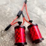 Close-up of two red cylindrical electronic components connected by black and red wires.