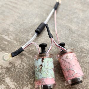 Two small, worn paint-splattered motorized devices connected by wires.