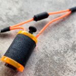 Close-up of a black and orange fishing line spool on a textured surface.