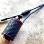 Close-up of a carbon fiber and metal vape pen part on a textured surface.