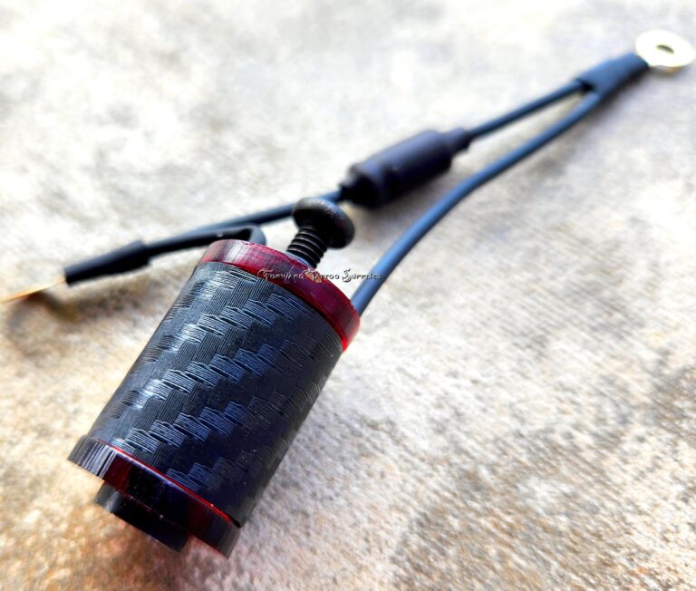 Close-up of a carbon fiber and metal vape pen part on a textured surface.