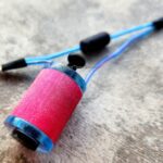 A bright pink spool of thread attached to a blue sewing tool.