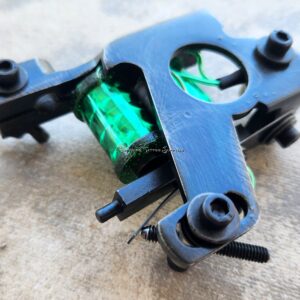 Close-up of a black tattoo machine with green coils.
