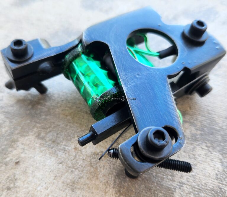 Close-up of a black tattoo machine with green coils.