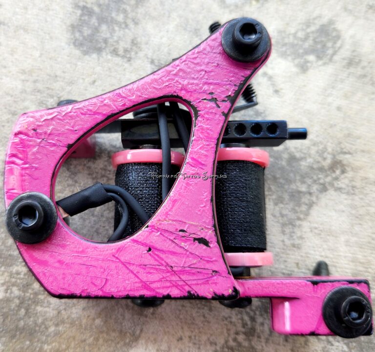 Pink tattoo machine on textured surface.