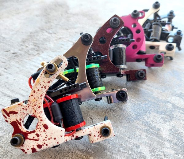 A row of colorful tattoo machines lined up on a surface.